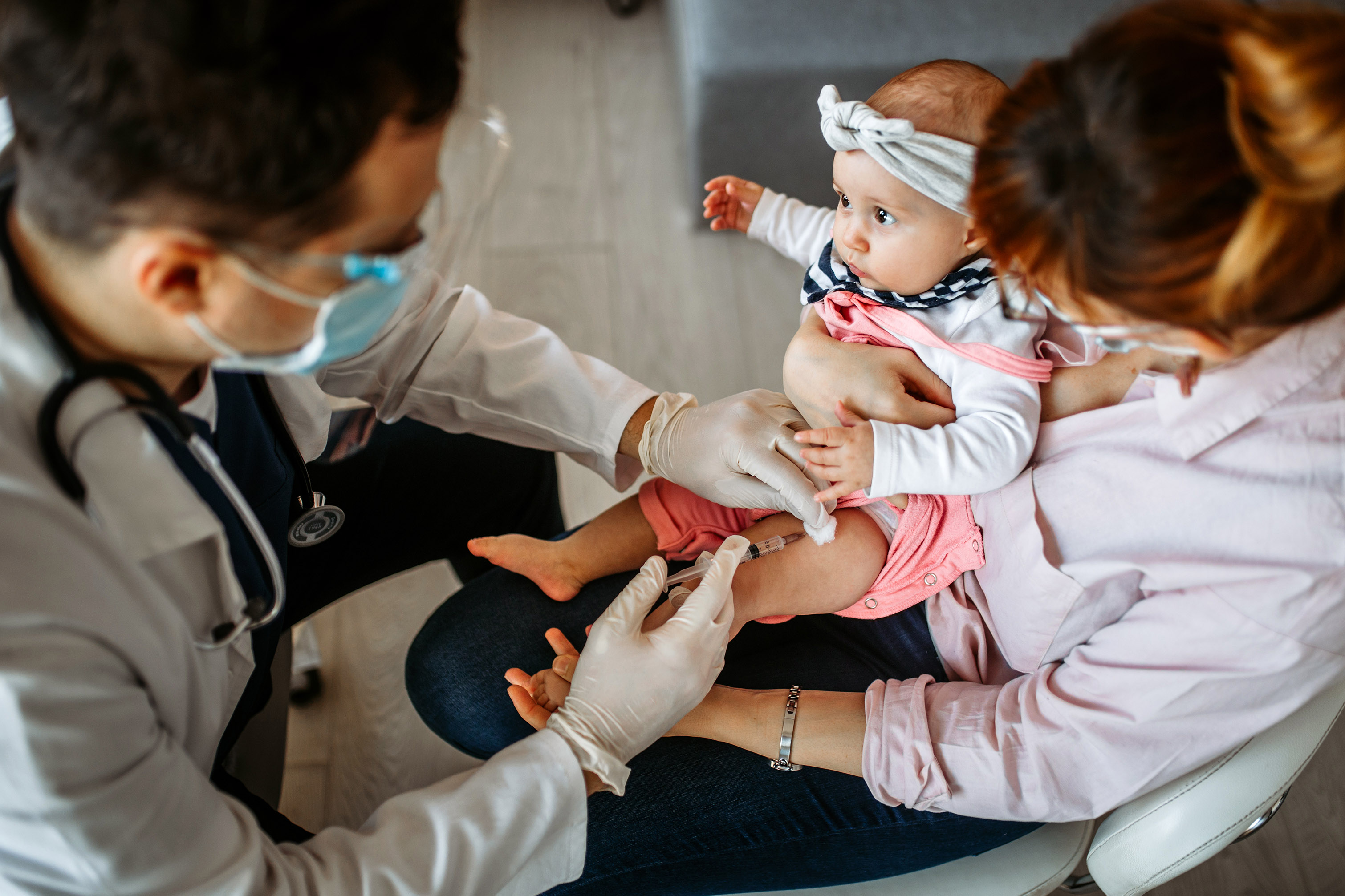 A woman holding her infant that is getting a vaccine from a doctor