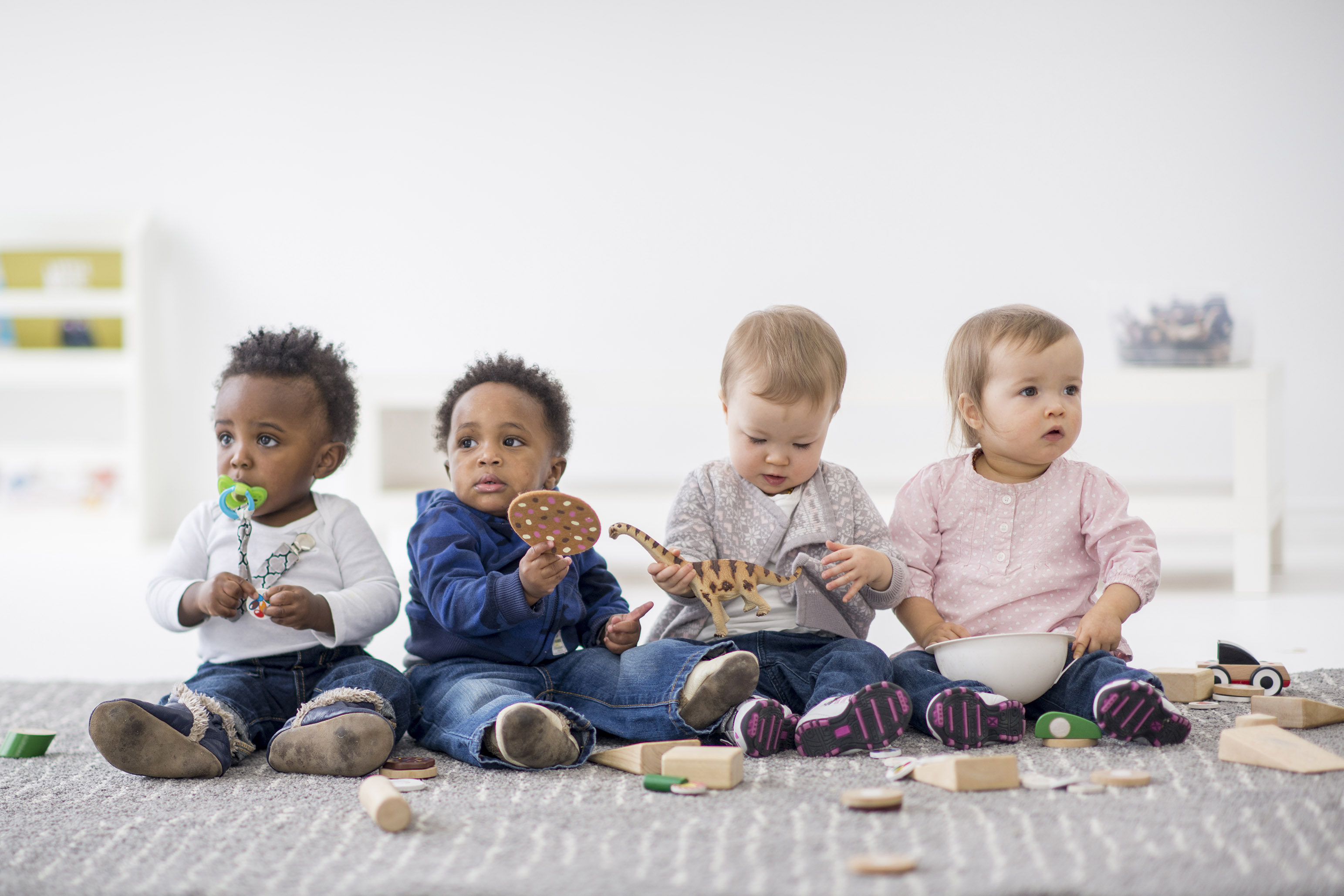 Four infants sitting on the floor playing with blocks