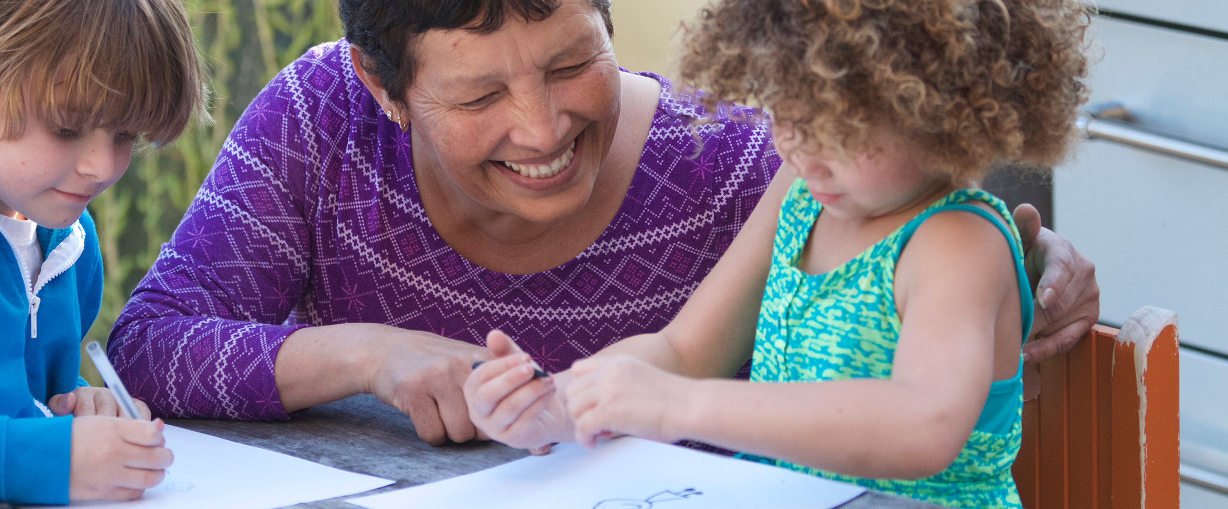 A child care provider helping two children with their artwork. 
