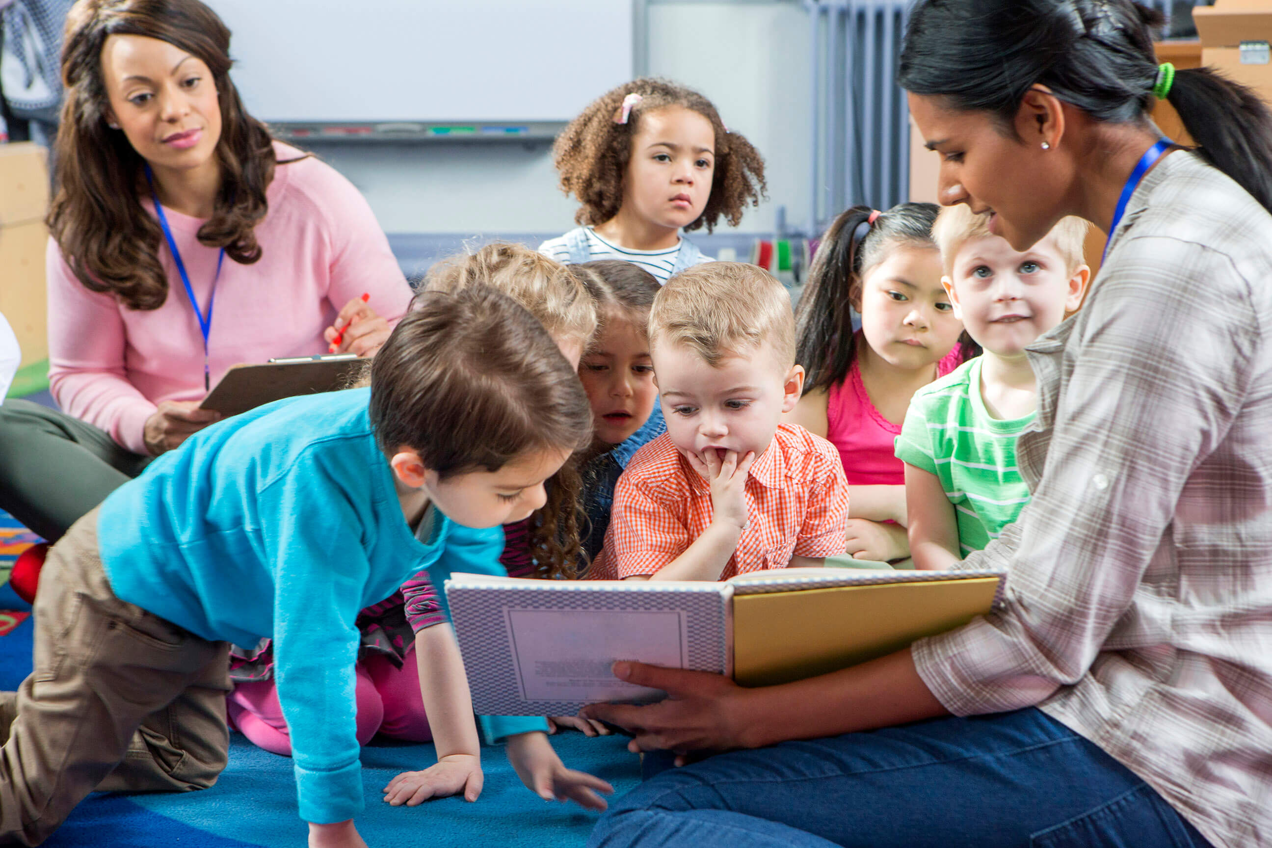 Child care provider sitting on the floor reading with students