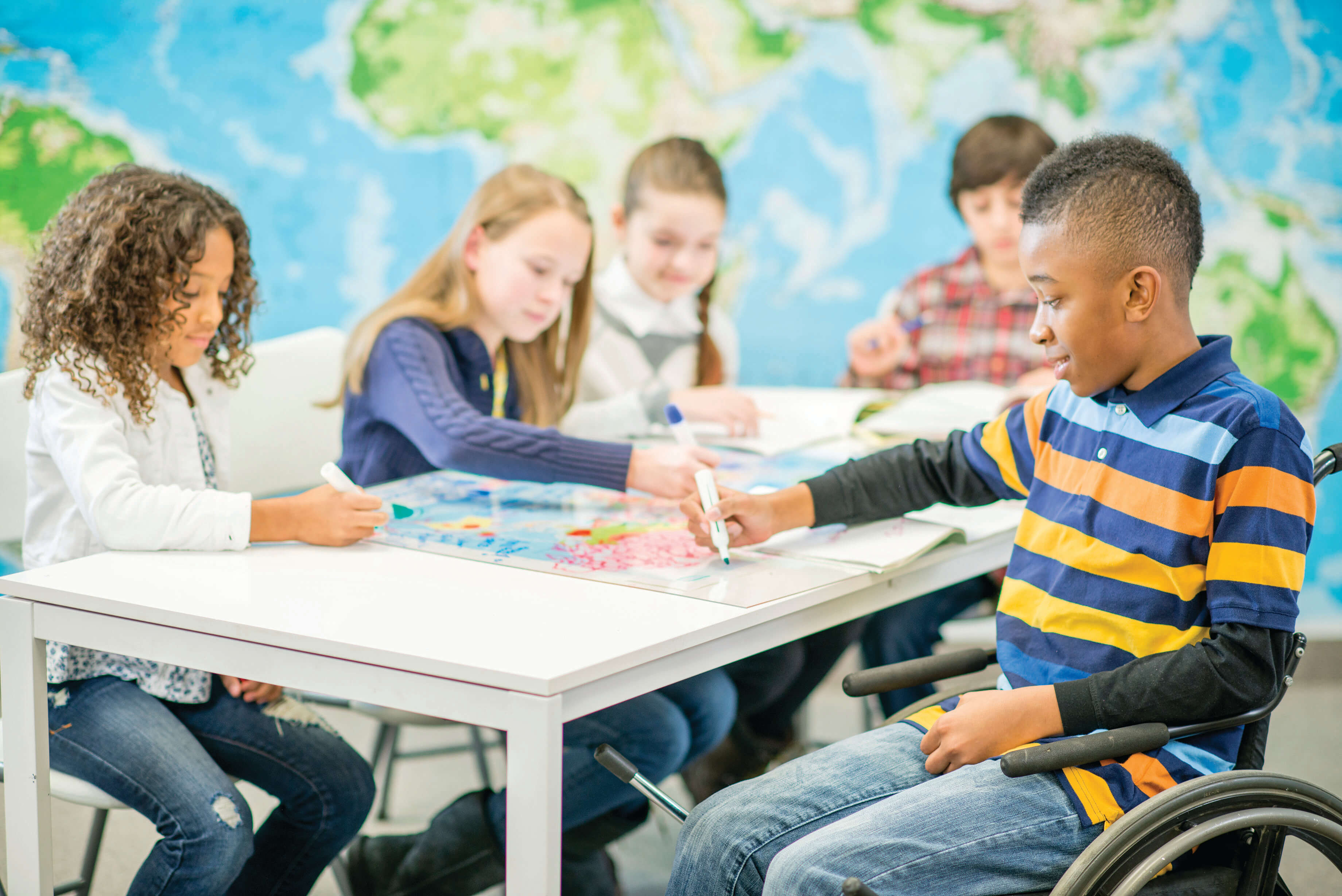 Five students, one in a wheelchair, sitting at a table while coloring